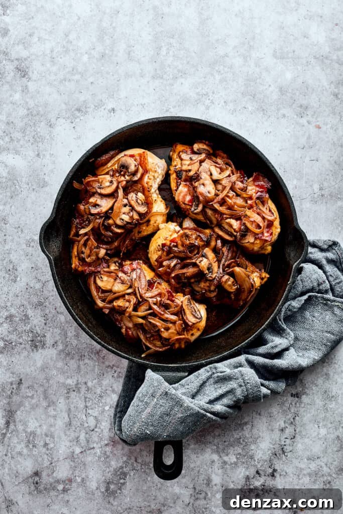 Four mushroom-topped chicken breasts in a cast iron skillet, ready for the next layer of toppings.