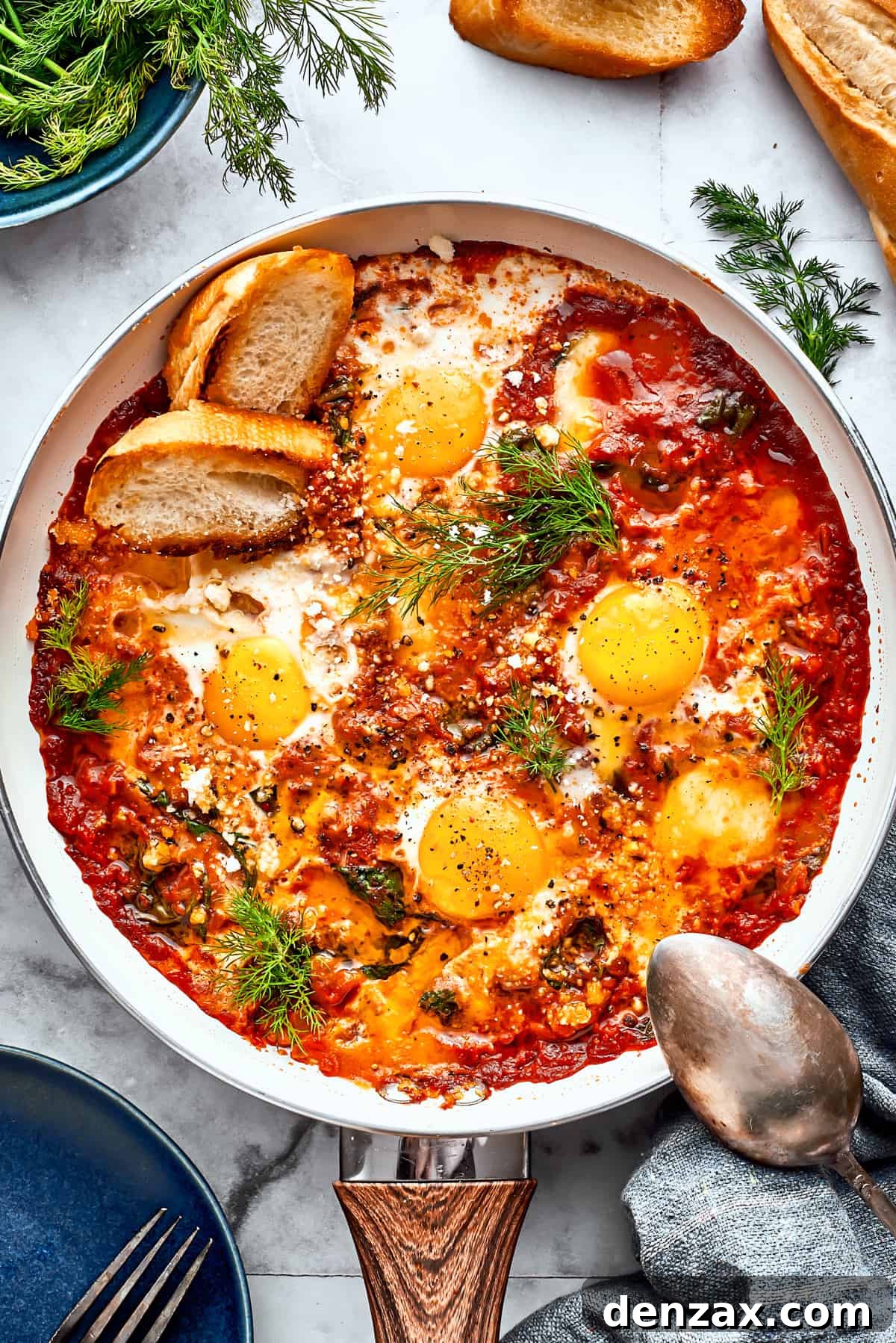 A cast iron skillet filled with bubbling Eggs in Purgatory, garnished with fresh parsley and served with golden-brown toasted bread slices on the side. A silver spoon rests on the skillet's edge.