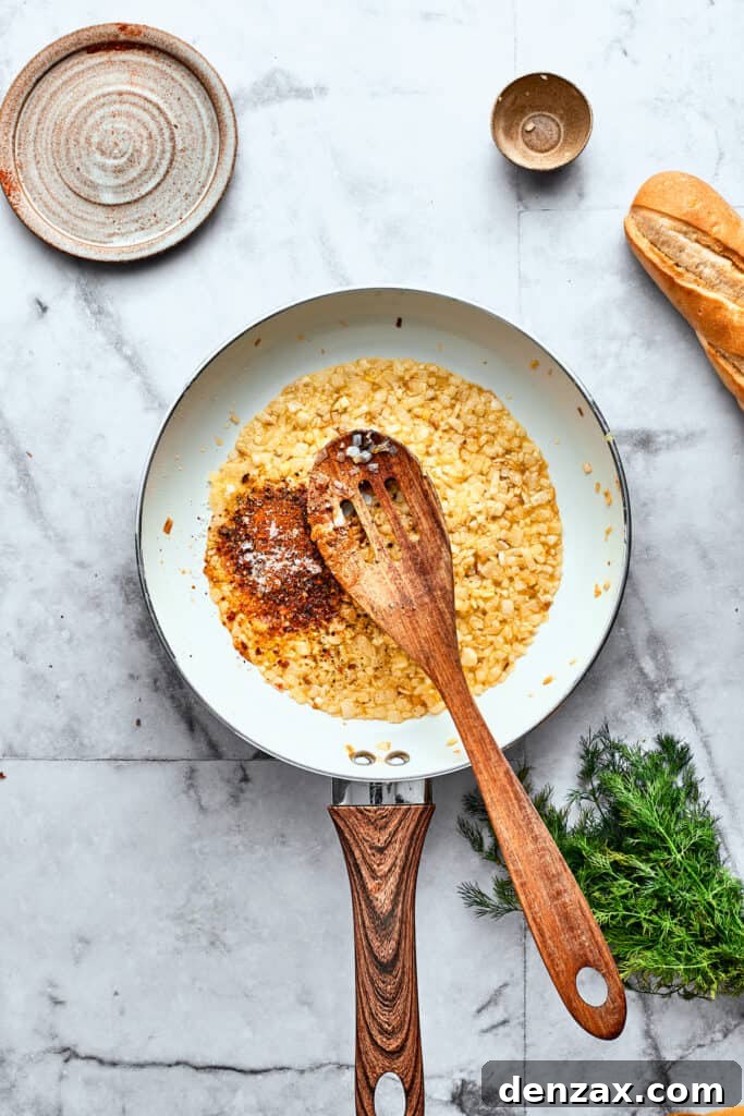 A wooden spoon gently stirs golden-brown diced onions and fragrant minced garlic in a large skillet, forming the savory base of the tomato sauce.