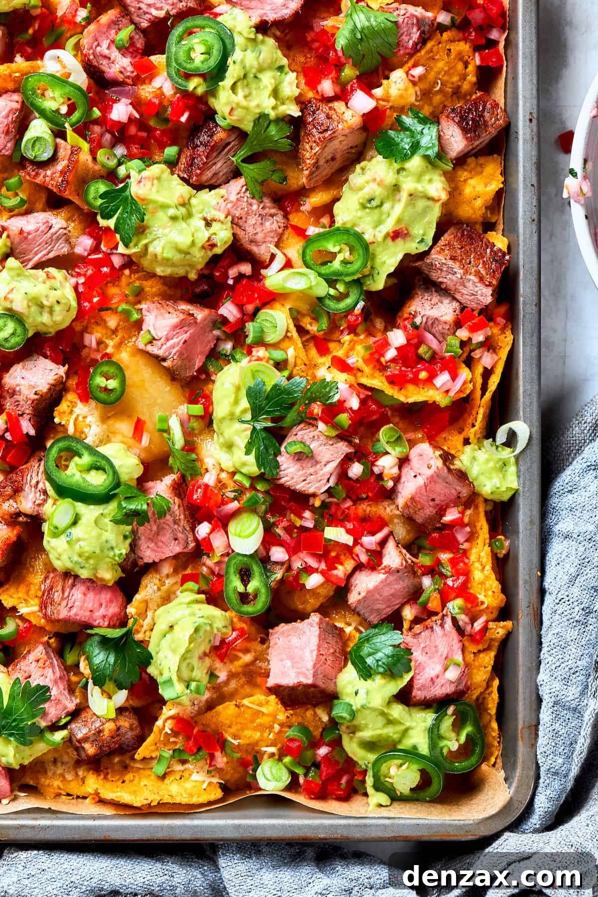 A big pan of steak nachos topped with guacamole and pico de gallo, showcasing vibrant colors and fresh ingredients.