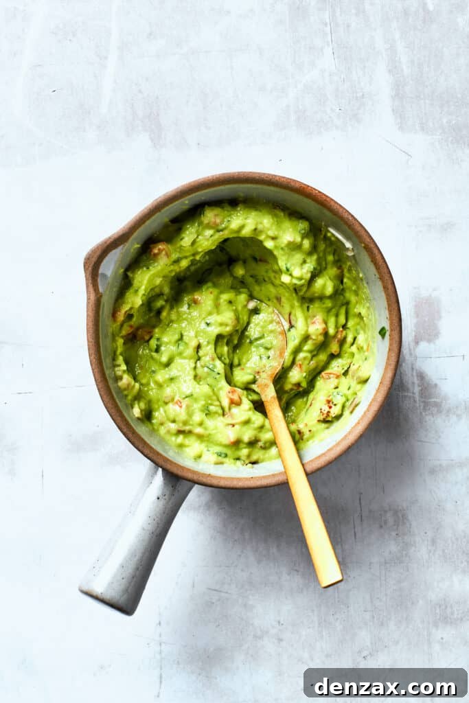 A wooden spoon stirs a bowl of guacamole.