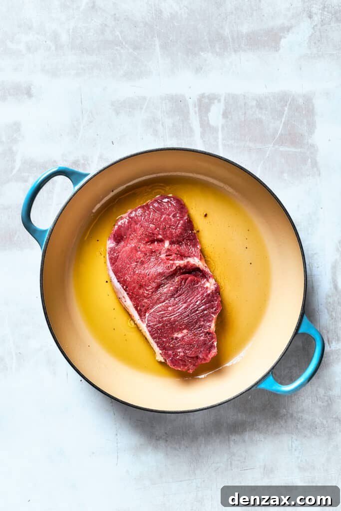 A piece of steak cooks in olive oil in a pan.