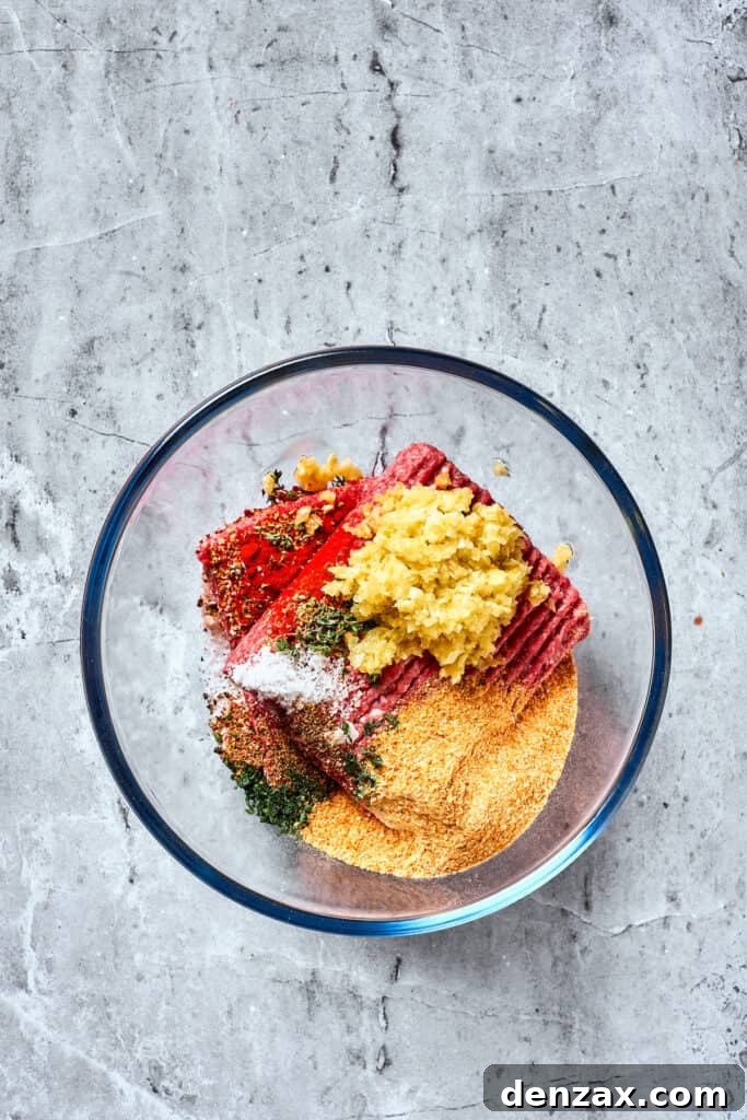 Meat, breadcrumbs, garlic, and spices are combined in a glass bowl.