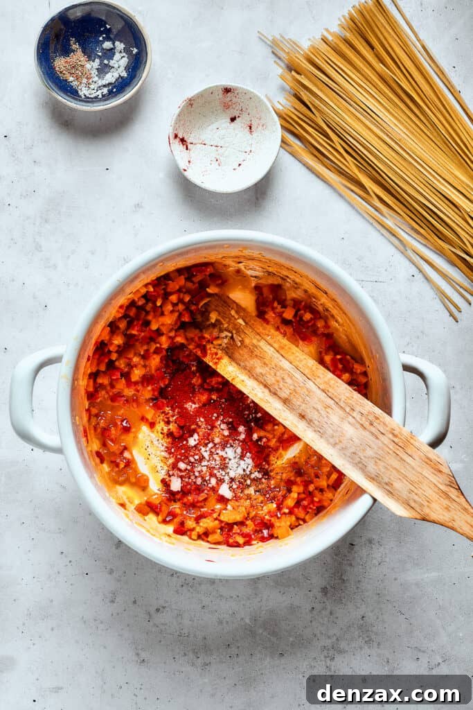 A wooden spoon stirs colorful vegetables, including carrots and bell peppers, in a large Dutch oven, creating the base for spicy chicken soup.