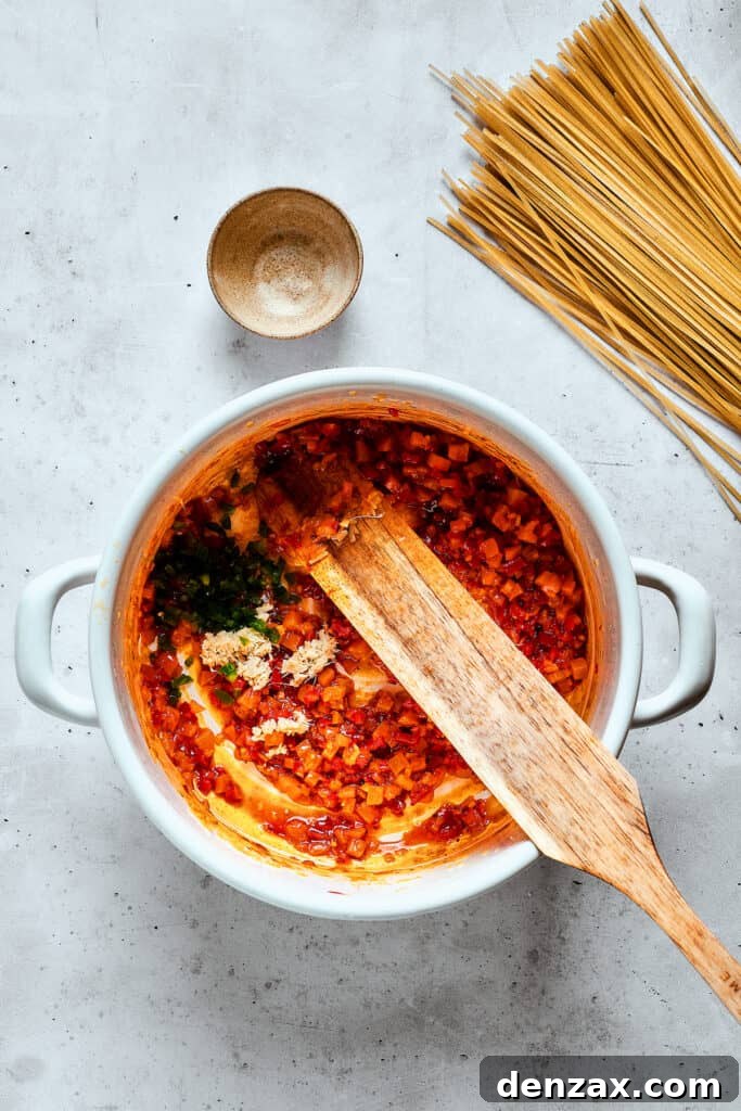 A wooden spoon continues to stir ingredients, including aromatic spices and vegetables, into a pot, building the rich flavors of spicy chicken soup.