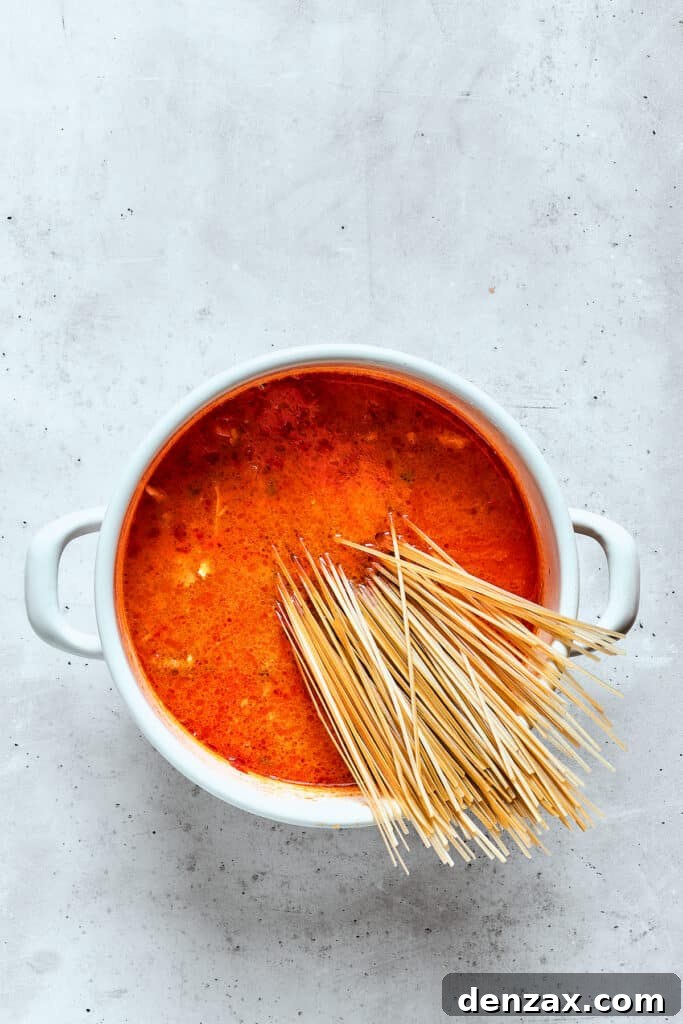 Close-up of thin rice noodles gently submerged into a pot of rich and creamy spicy chicken soup, absorbing the vibrant flavors.