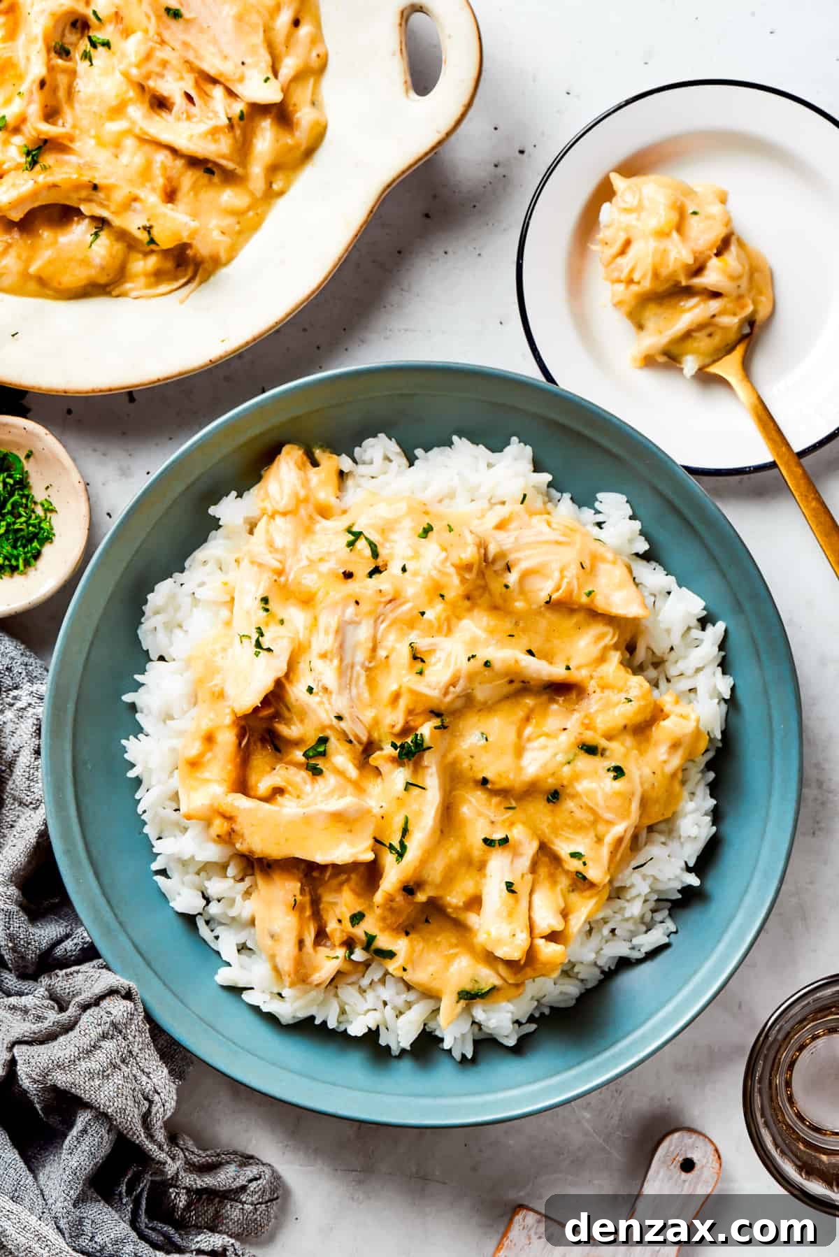 A serving of creamy slow cooker chicken and gravy nestled over a bed of fluffy white rice in a beautiful blue bowl, garnished with fresh parsley.