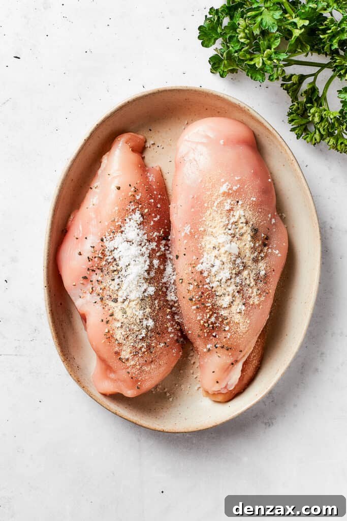 Two boneless, skinless chicken breasts seasoned generously with salt, pepper, and garlic powder, ready for cooking in an oval serving dish.