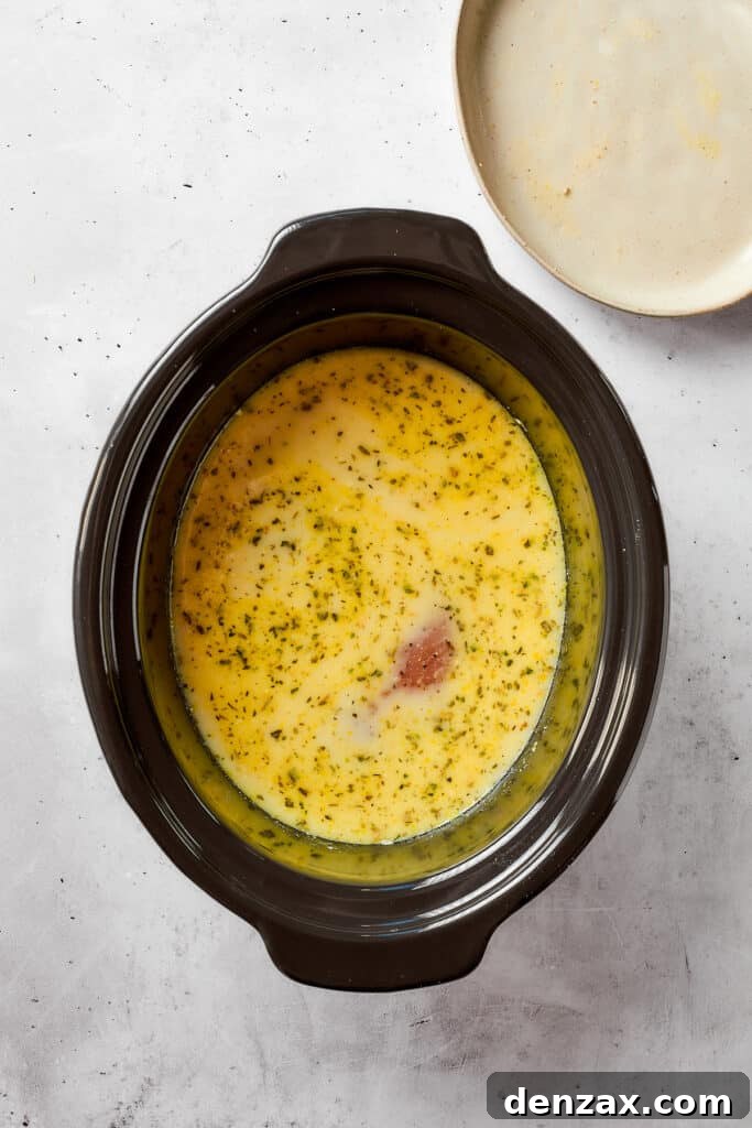 Seasoned chicken breasts are carefully placed into the creamy gravy mixture inside a slow cooker, ready for cooking.
