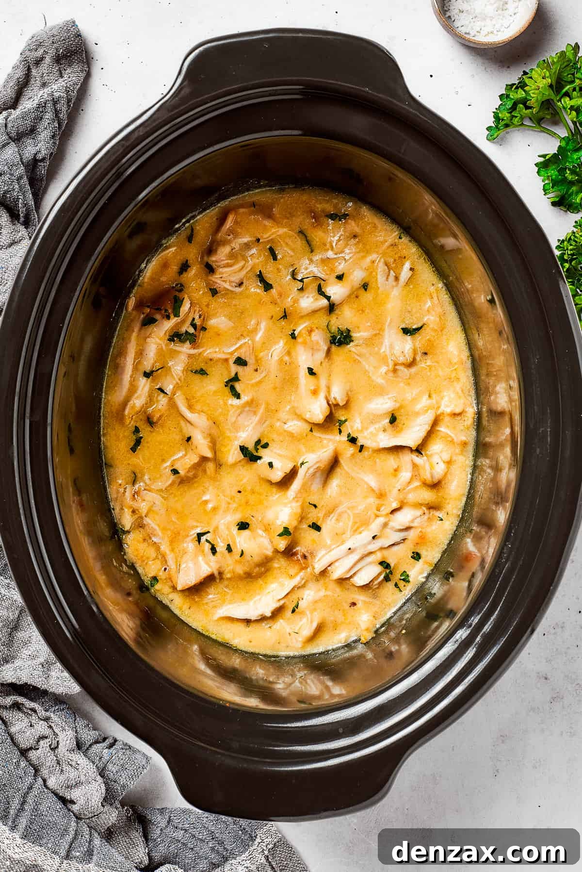 A close-up view of creamy chicken and gravy simmering perfectly in a black slow cooker, highlighting the rich texture of the sauce and tender chicken pieces.