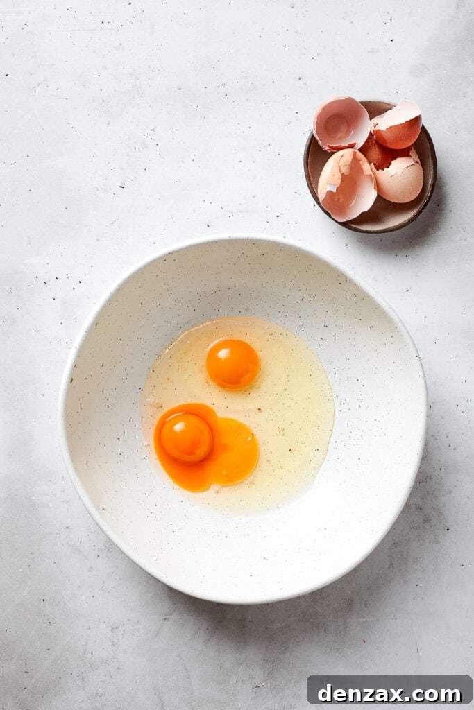 Two eggs and an egg yolk in a white bowl.