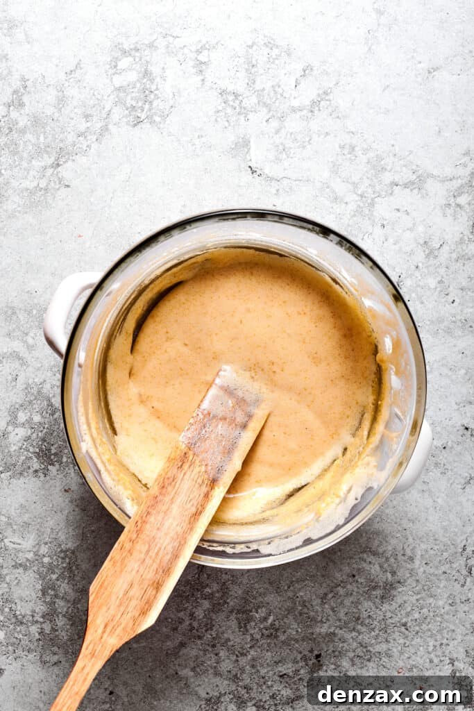 A spatula stirs the egg and sugar mixture in a bowl set over simmering water, ensuring even cooking.