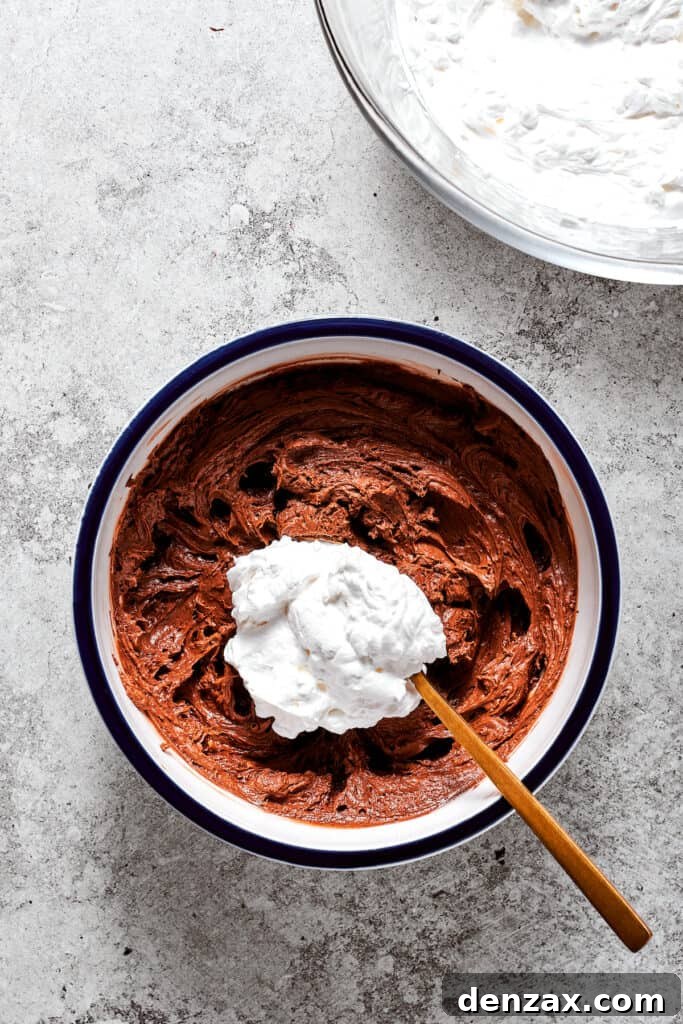 A spoonful of whipped cream is gently folded into the chocolate filling in a bowl, creating a light and airy texture.