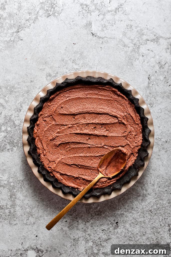 A spoon smooths the rich French silk pie filling into the prepared Oreo cookie crust, creating an even layer.