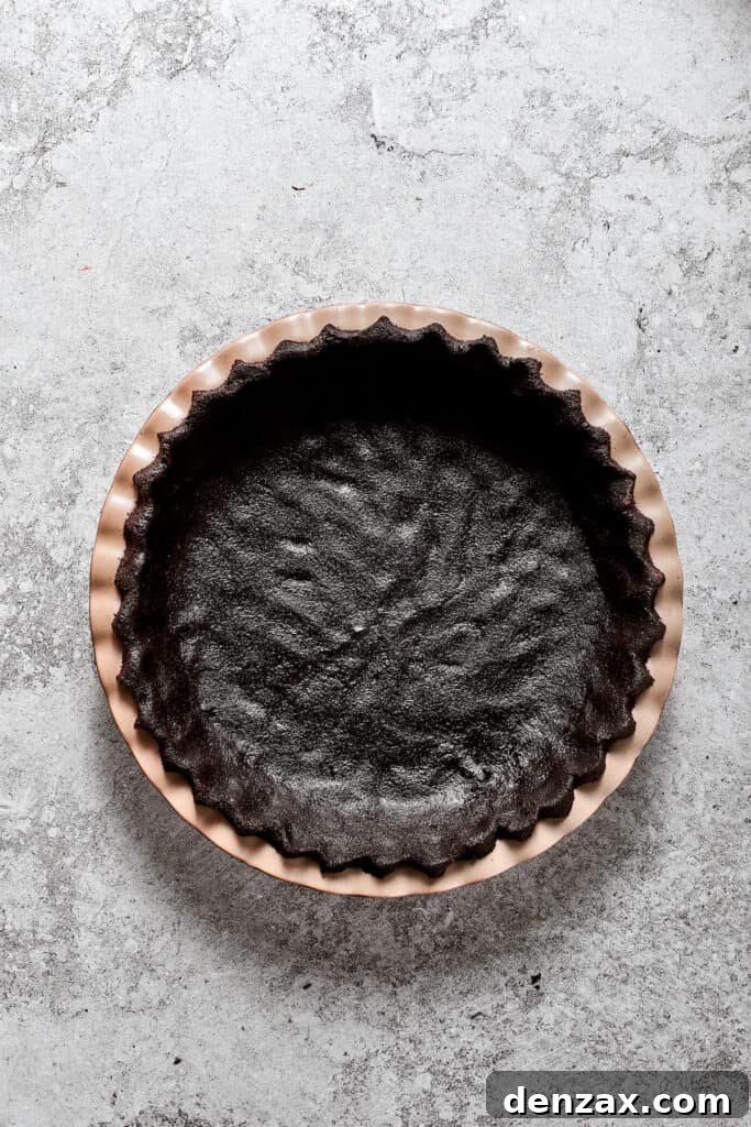 An evenly pressed Oreo cookie crust lining a pie pan, chilling in the refrigerator.
