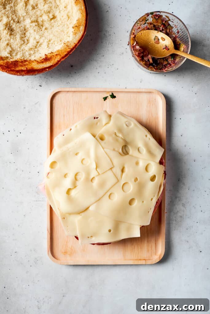Slices of Swiss cheese are meticulously placed on the sandwich layers, contributing to the rich and creamy filling of the muffaletta.