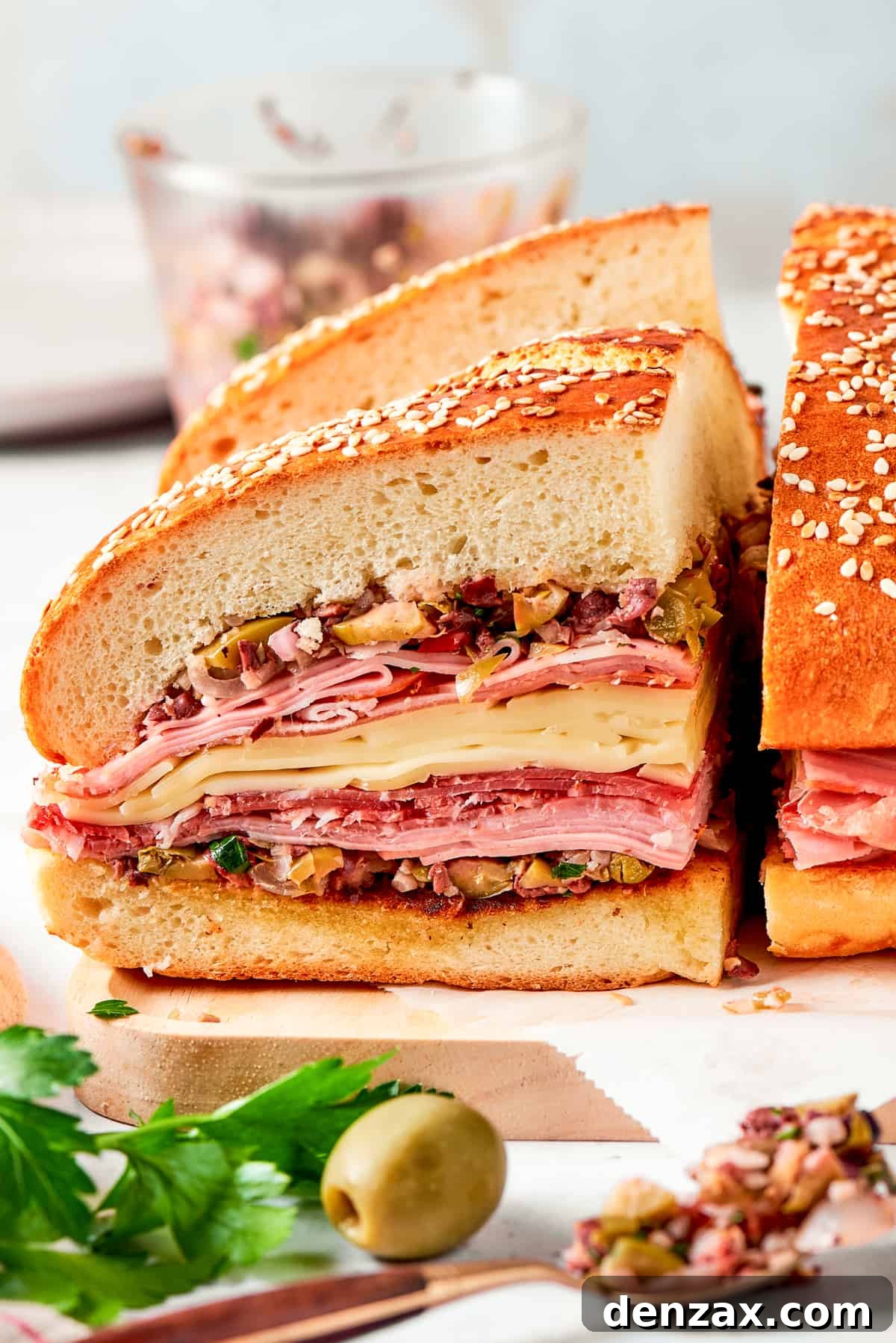 Two generous pieces of a tall, perfectly assembled muffaletta sandwich rest on a cutting board, proudly displaying the vibrant layers of meats, cheeses, and olive salad.