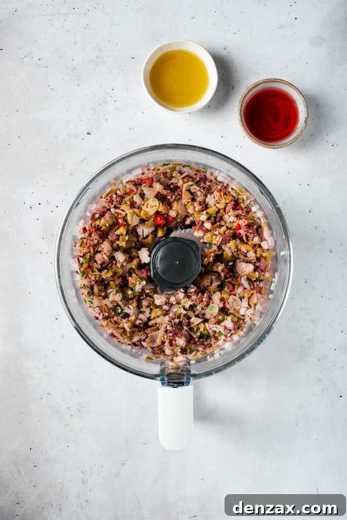 The olive salad mixture is finely pulsed in a food processor to a coarse, textured consistency, showcasing its colorful components.