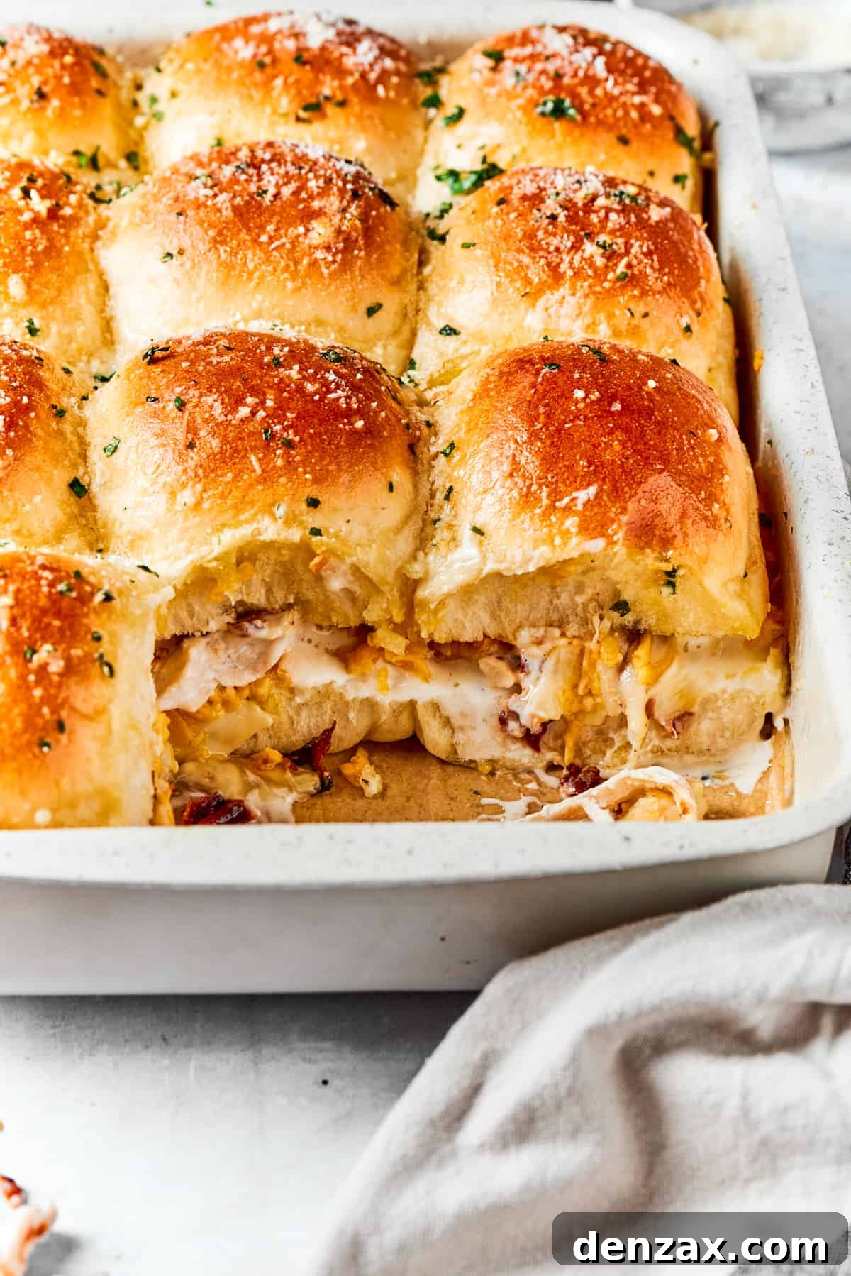 Close-up of baked chicken sliders in a baking dish, with two sliders pulled apart to show the melted cheese, chicken, and bacon filling inside.