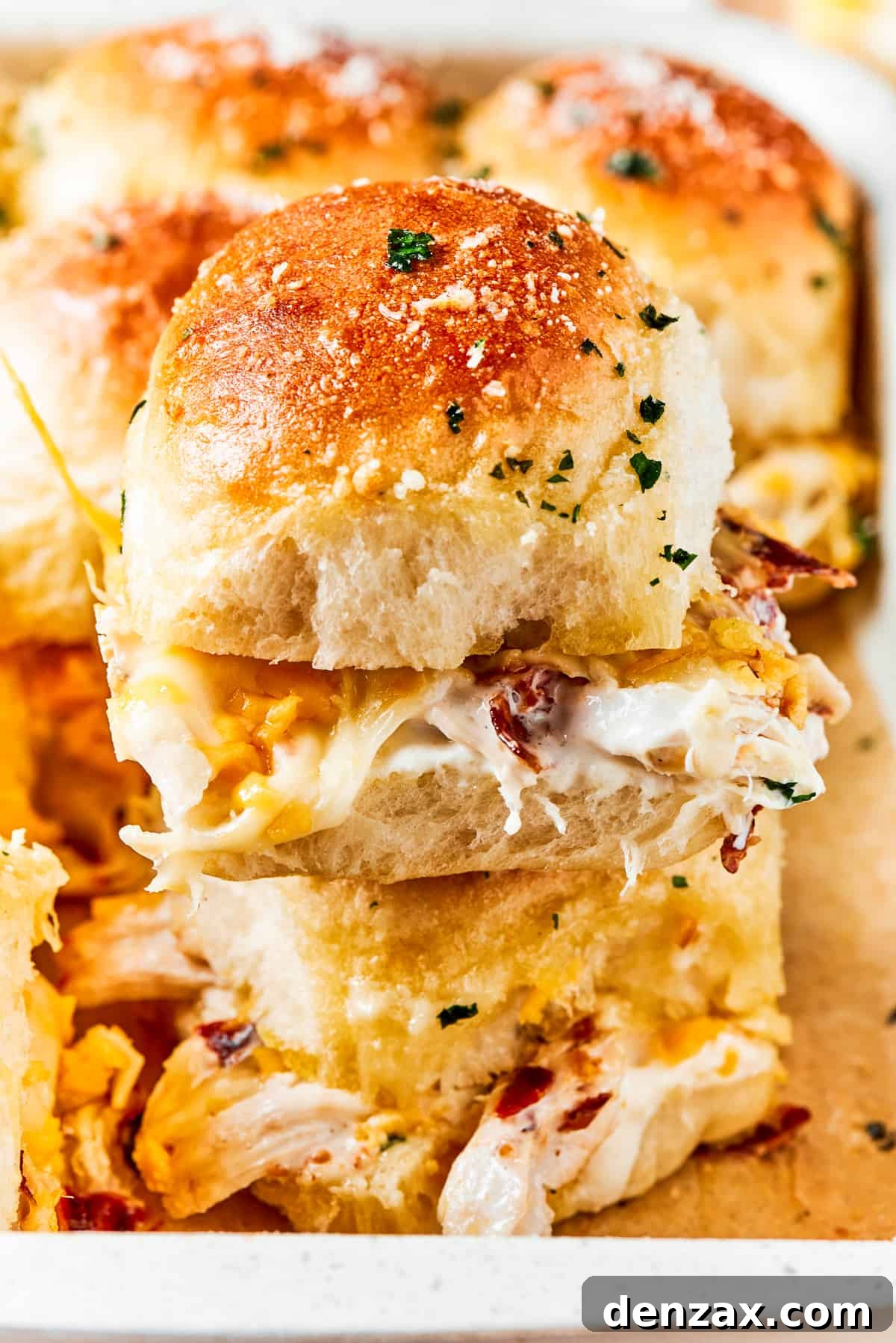 Two chicken bacon ranch sliders stacked on a cutting board, showing the layers of chicken, bacon, ranch, and melted cheese, with fresh parsley garnish.