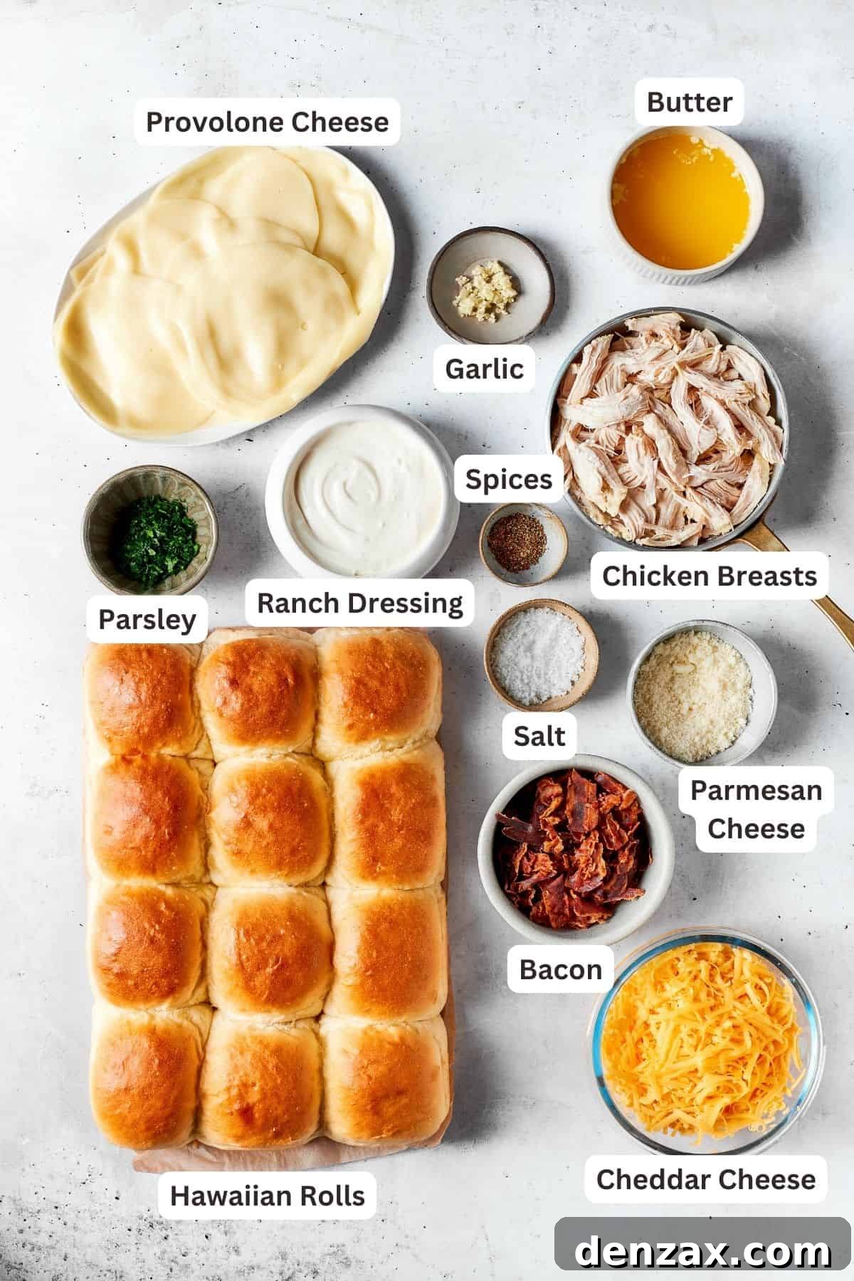 All the fresh ingredients laid out for making chicken bacon ranch sliders: Hawaiian sweet rolls, provolone, cheddar, and Parmesan cheeses, shredded chicken, crispy bacon, ranch dressing, fresh parsley, garlic, and butter.