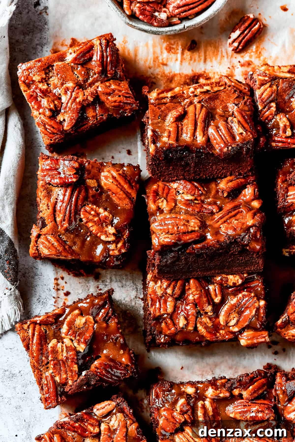 Perfectly cut Pecan Pie Brownies lined on parchment paper, showcasing the rich chocolate base and the glossy, nut-filled topping.