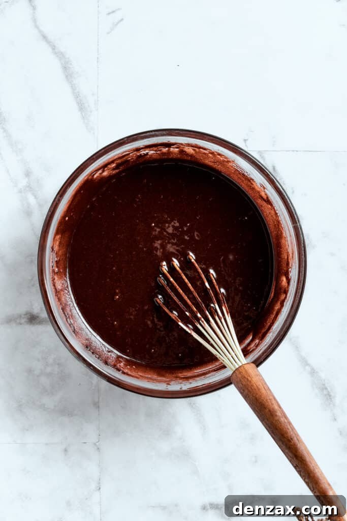A whisk smoothly blends a bowl of rich brownie batter until perfectly combined and lump-free.
