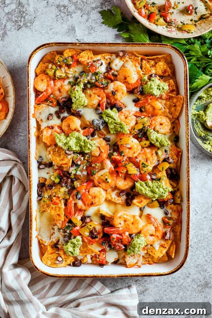 Guacamole is dolloped onto the tray of shrimp nachos.