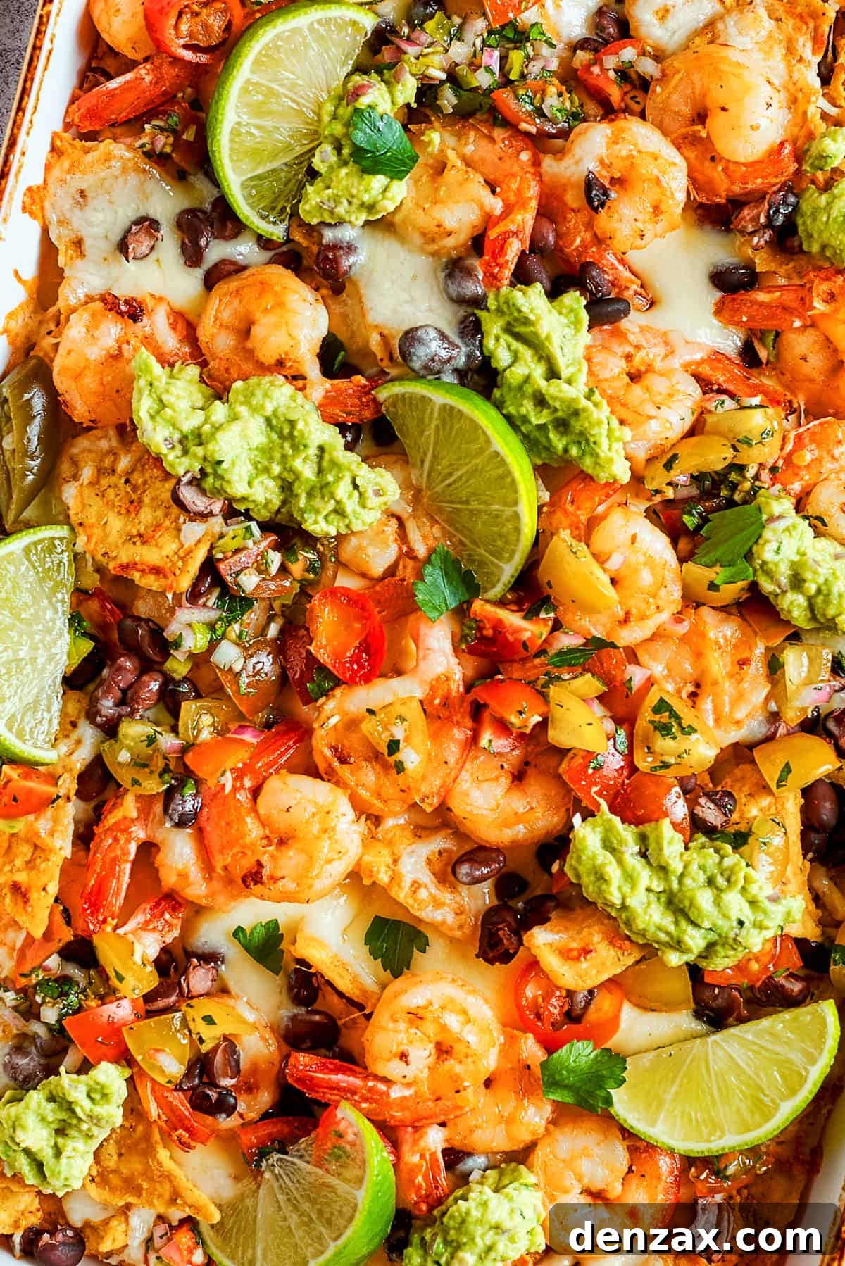 Tortilla chips topped with shrimp, cheese, black beans, tomatoes, and a garnish of guacamole and slices of lime.