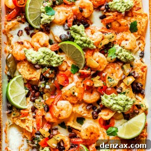 Nacho chips topped with shrimp, cheese, black beans, tomatoes, and a garnish of guacamole and slices of lime.