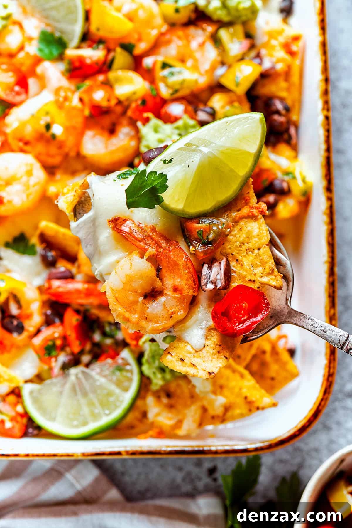 A spoon lifts out nachos from a baking dish.