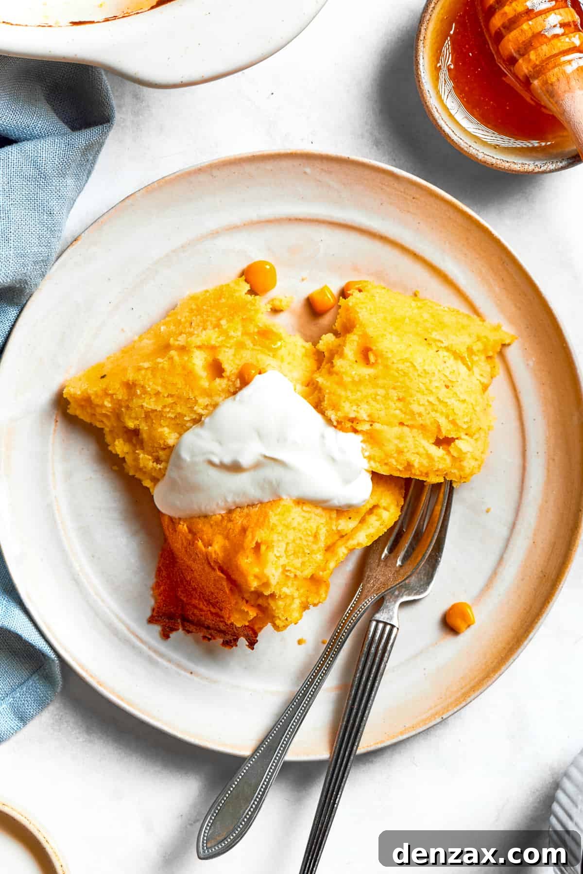 A single serving of Spoon Bread, topped with a dollop of creamy sour cream, rests on a white plate, ready to be enjoyed.