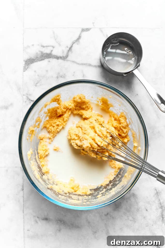 Whole milk is gradually being whisked into the cornmeal mixture, ensuring a smooth, lump-free batter for Spoon Bread.