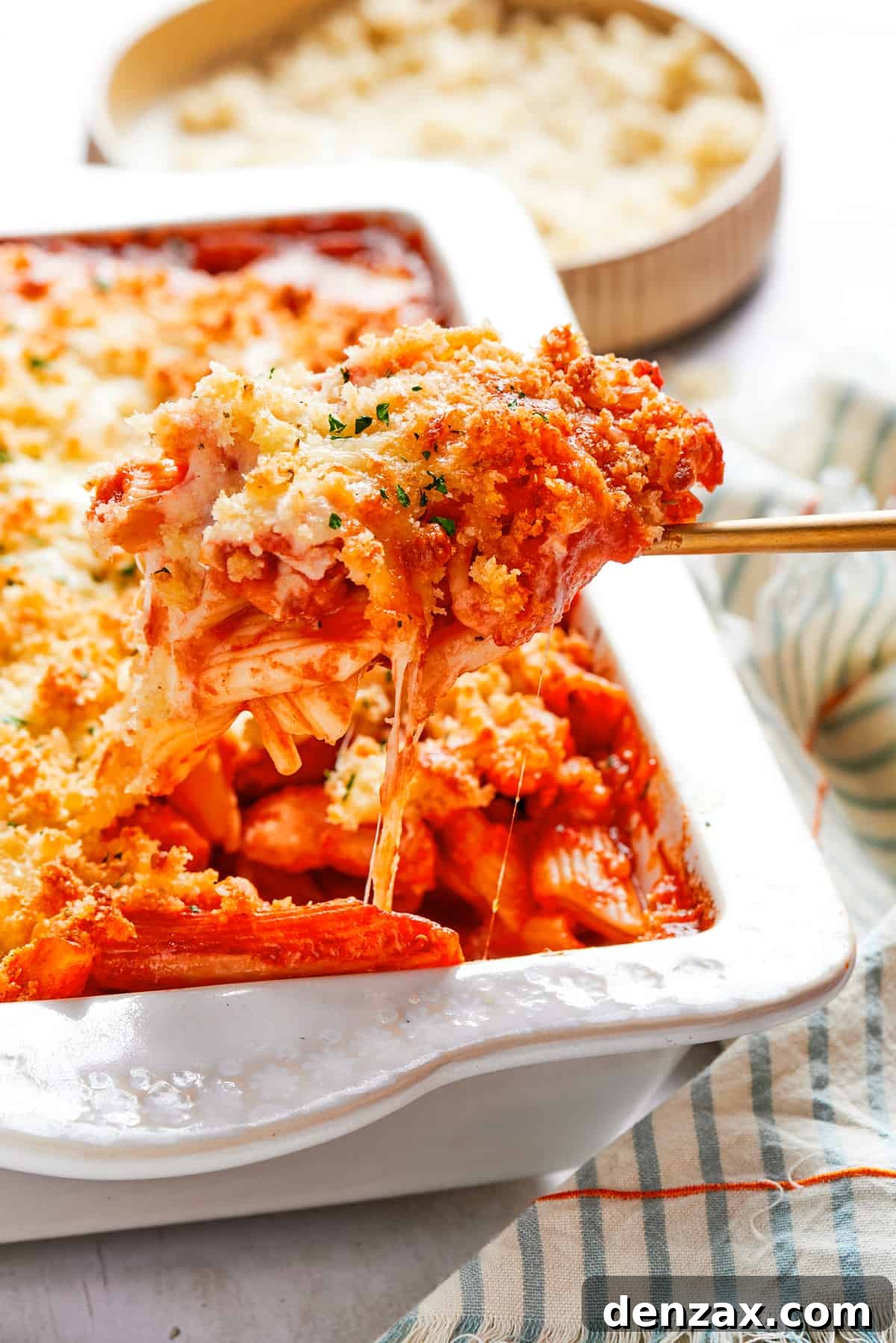 A spoon is pulling out chicken pasta from a baking dish.