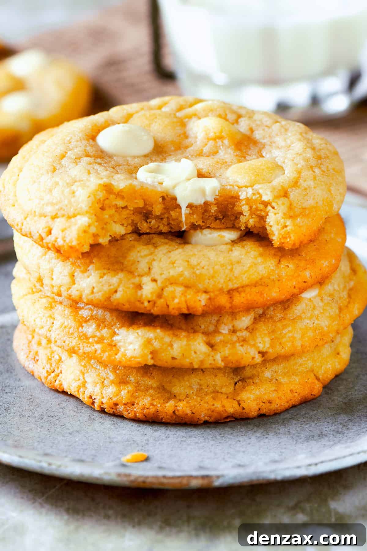 Four perfectly stacked white chocolate chip cookies on a small white plate, ready to be enjoyed.