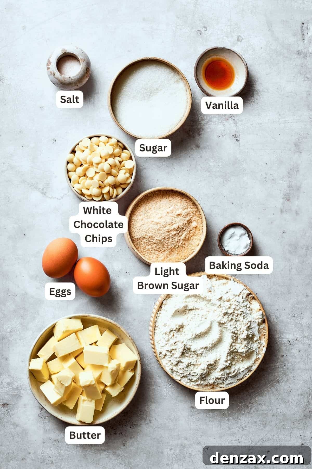 Ingredients for white chocolate chip cookies are neatly displayed and portioned: white chocolate chips, all-purpose flour, unsalted butter, granulated sugar, light brown sugar, baking soda, large eggs, vanilla extract, and salt.