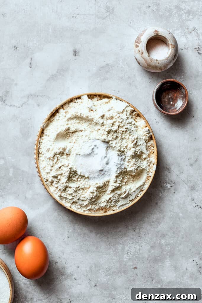 The dry mix of flour, salt, and baking soda for white chocolate chip cookie dough is being added to a bowl, ready to be combined.