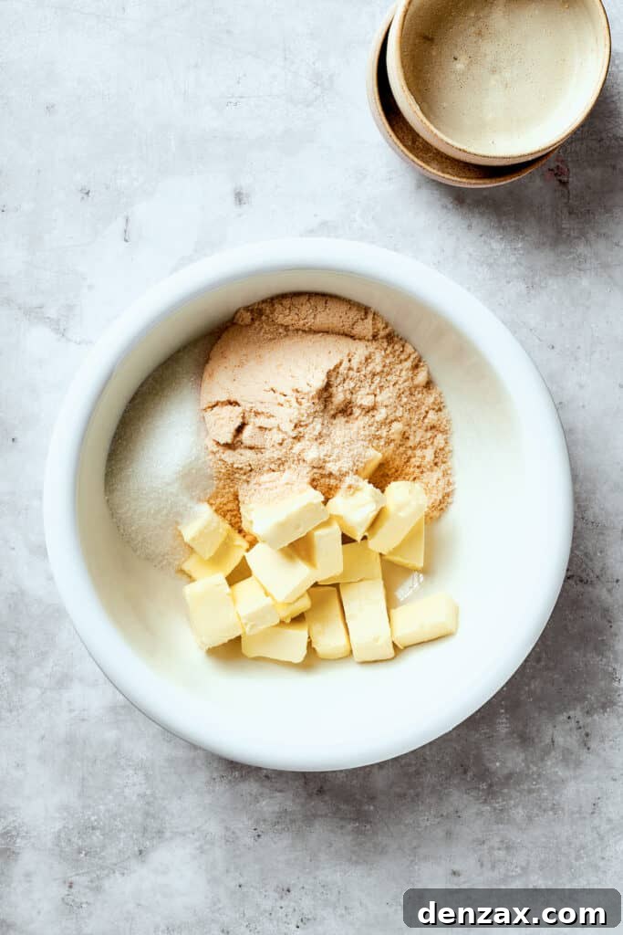 Softened butter, granulated sugar, and light brown sugar are combined in a large white mixing bowl, ready for creaming.
