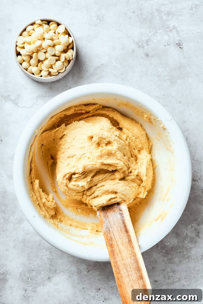 The cookie dough is being gently stirred in a bowl after the dry ingredients have been added, just until combined.