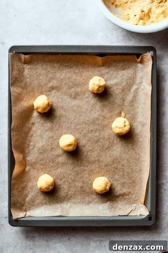 Balls of white chocolate chip cookie dough are evenly spaced on a lined baking sheet, ready for the oven.