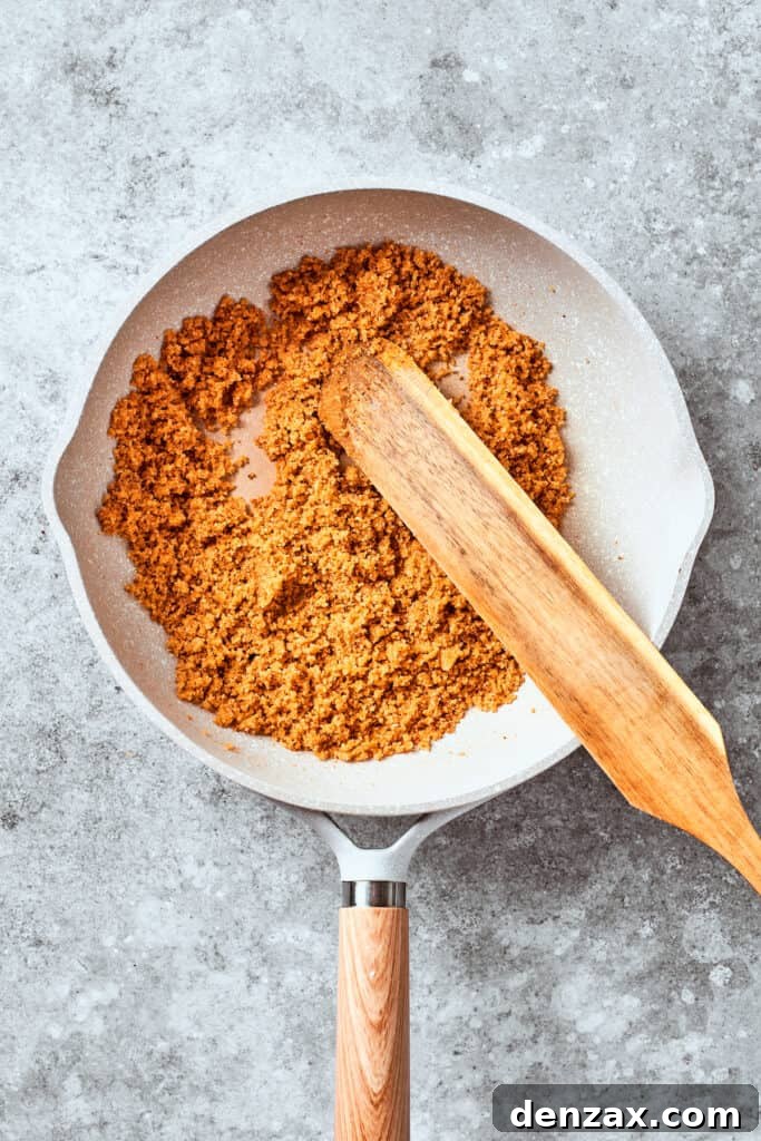 A wooden spoon mixes up the breadcrumbs in a pan.