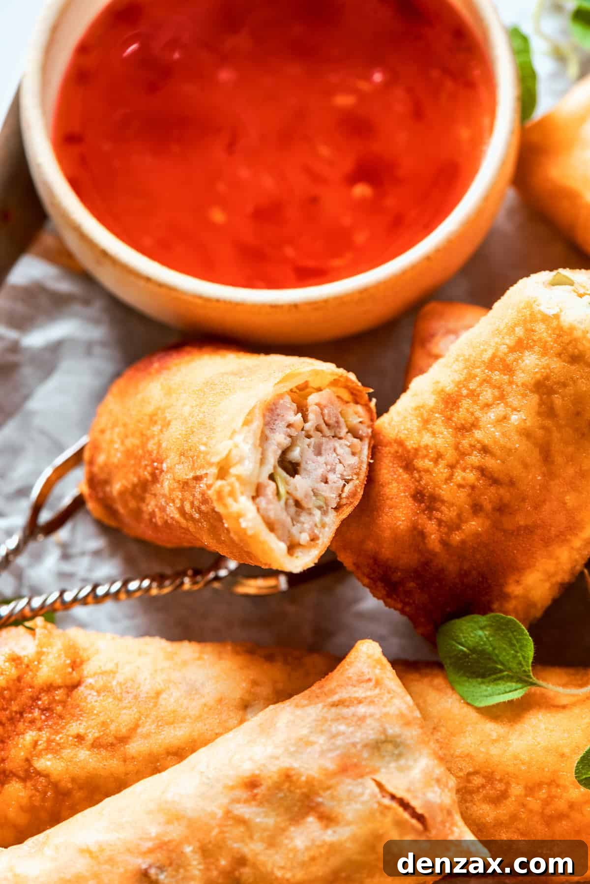 A vibrant display of crispy chicken egg rolls, golden brown and perfectly fried, are artfully arranged next to a small, enticing bowl of rich red dipping sauce, ready to be enjoyed.