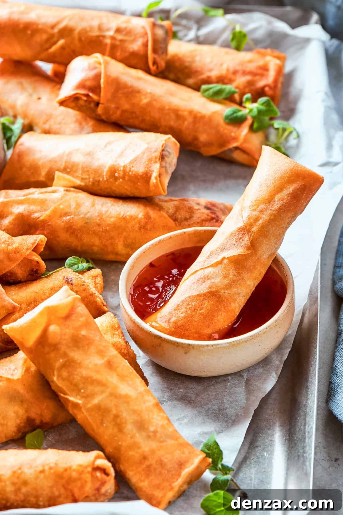 A perfectly fried, golden-brown chicken egg roll is being dipped into a small bowl of savory sauce, with more crispy egg rolls artfully arranged around it on a serving platter, highlighting their deliciousness.