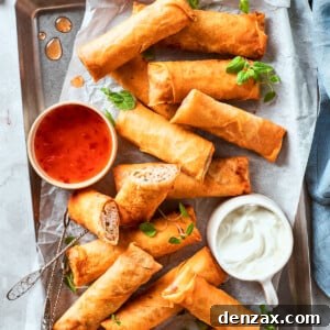 A serving platter laden with golden, crispy chicken egg rolls. Accompanying them are two small bowls, one filled with a vibrant red dipping sauce and the other with a creamy white sauce, inviting a delightful culinary experience.