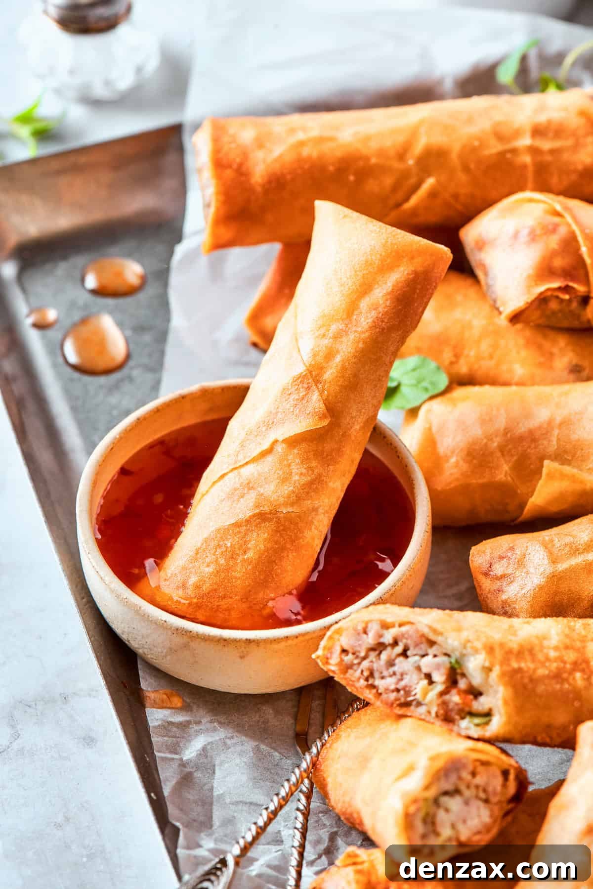 A close-up shot of crispy chicken egg rolls, some whole and some expertly sliced in half, revealing their savory filling. They are elegantly presented with a small bowl of dipping sauce, into which one of the egg rolls is being dipped, promising a delightful bite.
