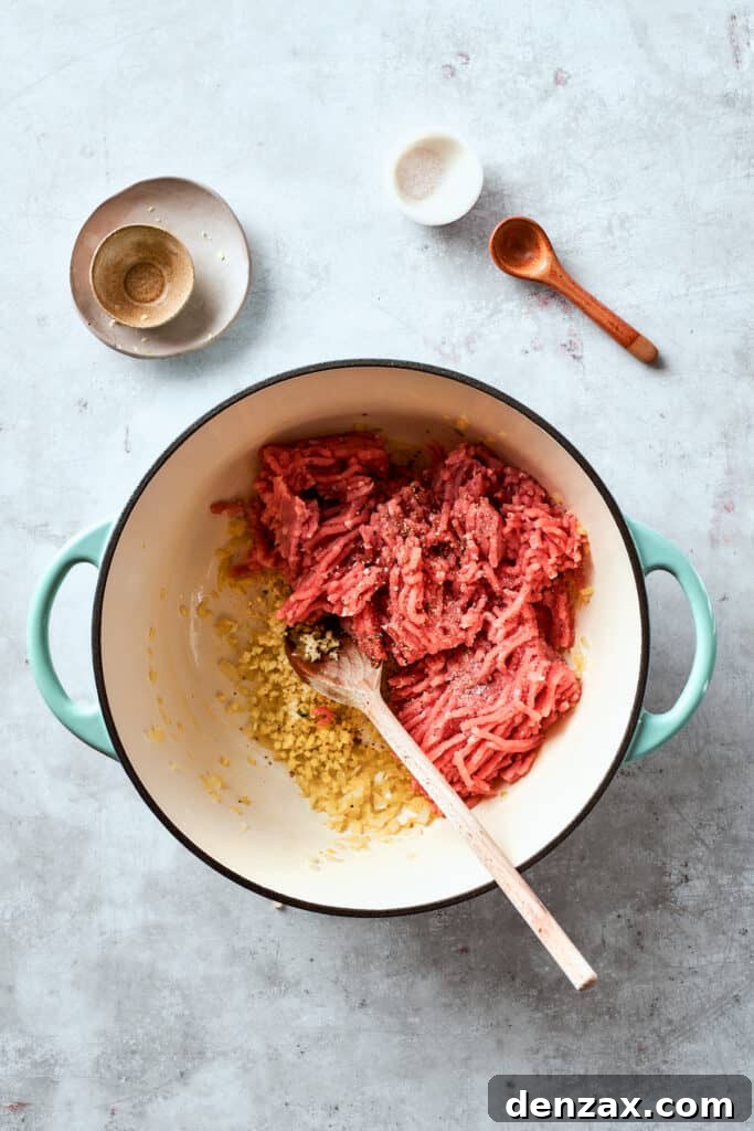 Fresh ground chicken is carefully added to a hot pan, ready to cook and brown as the first step in preparing the savory filling for chicken egg rolls.