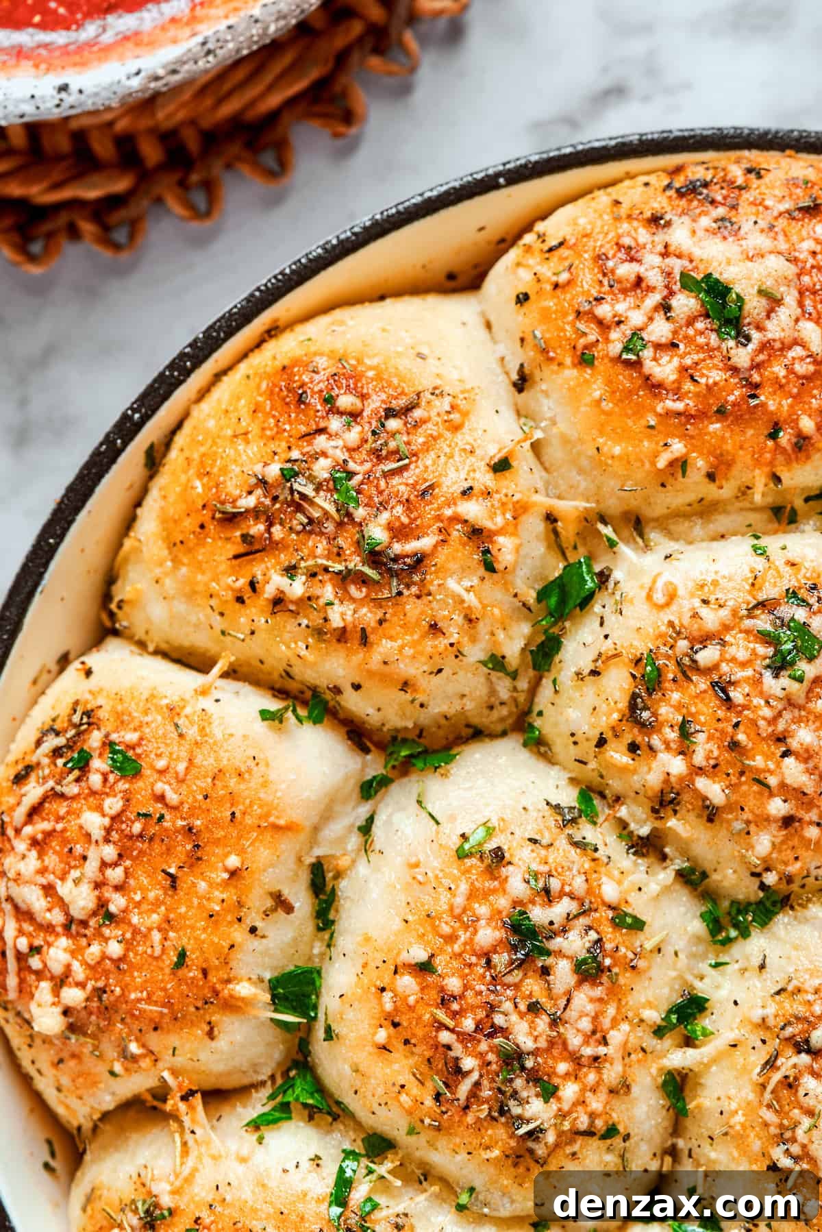 Half of a skillet filled with freshly baked pizza bites, generously topped with fresh green herbs, highlighting their golden crusts and inviting aroma.