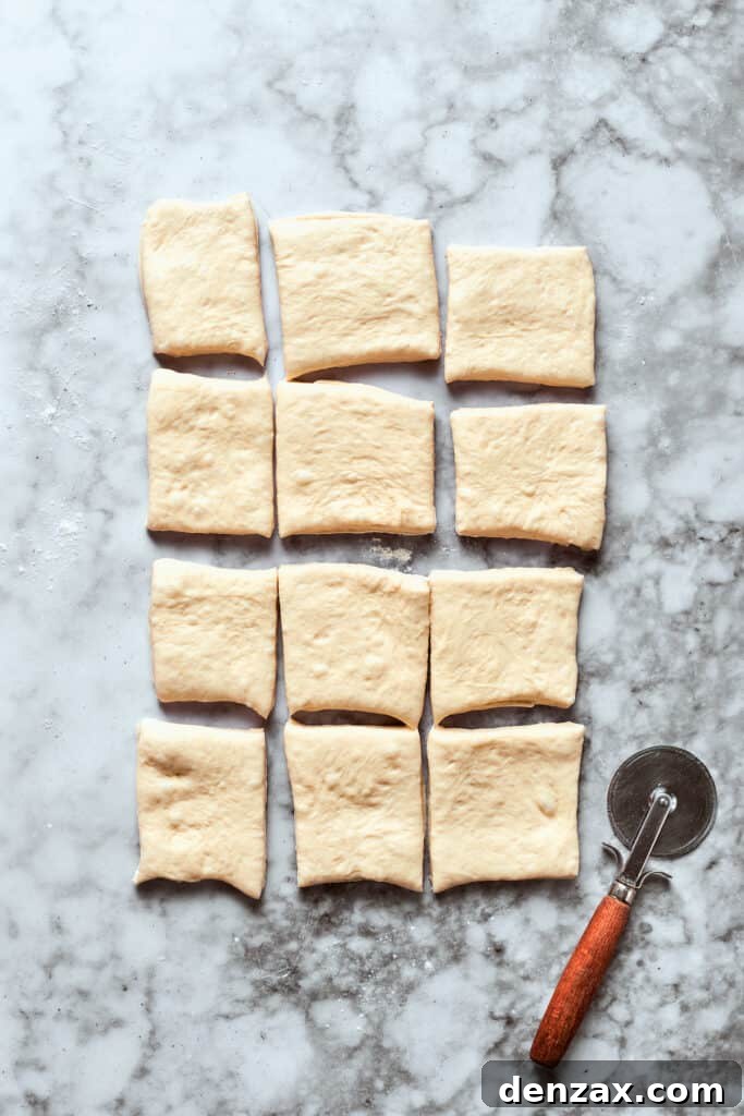The rolled-out pizza dough is neatly cut into twelve equal squares, ready for filling.