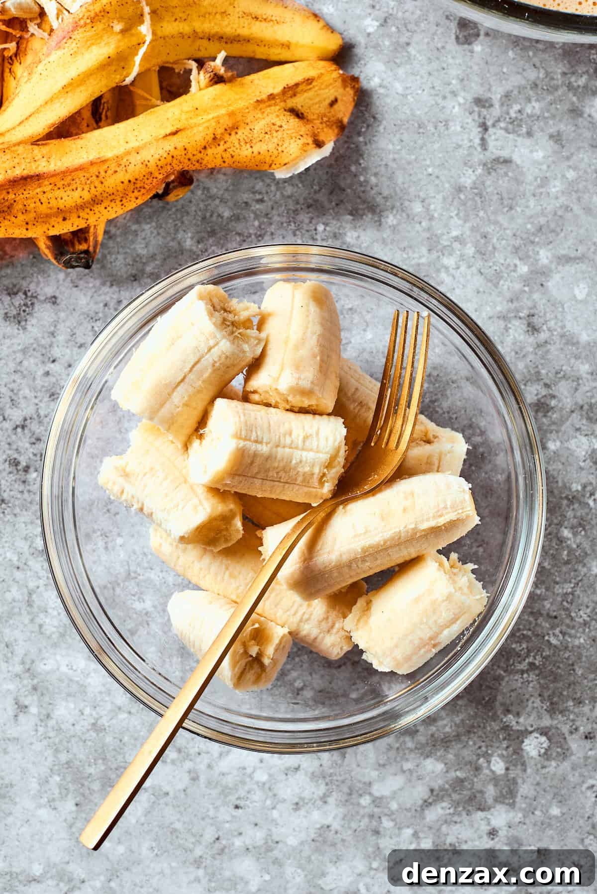 A bowl of perfectly ripened, soft bananas, already peeled, awaits mashing with a sturdy fork, signifying the next step in preparing the banana bread.