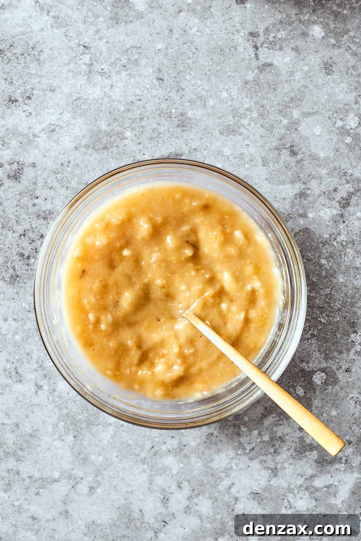Creamy mashed bananas are gently folded into the wet ingredient mixture in a bowl, ensuring thorough incorporation for a rich and moist banana bread batter.
